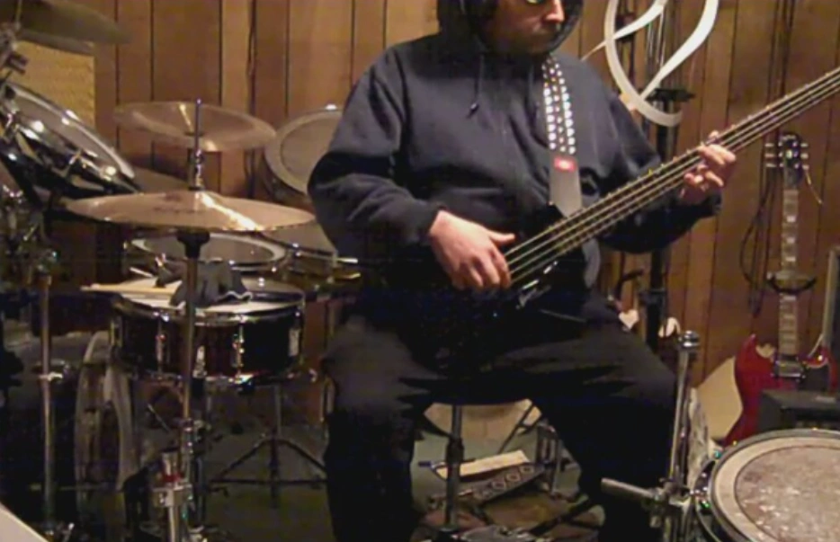 Larry sitting behind his drums playing bass.